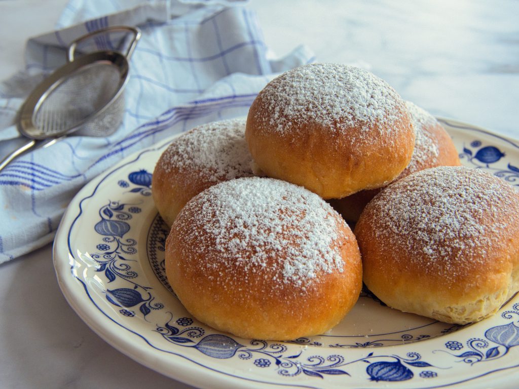 Fünf Krapfen mit Puderzucker auf einem Teller.