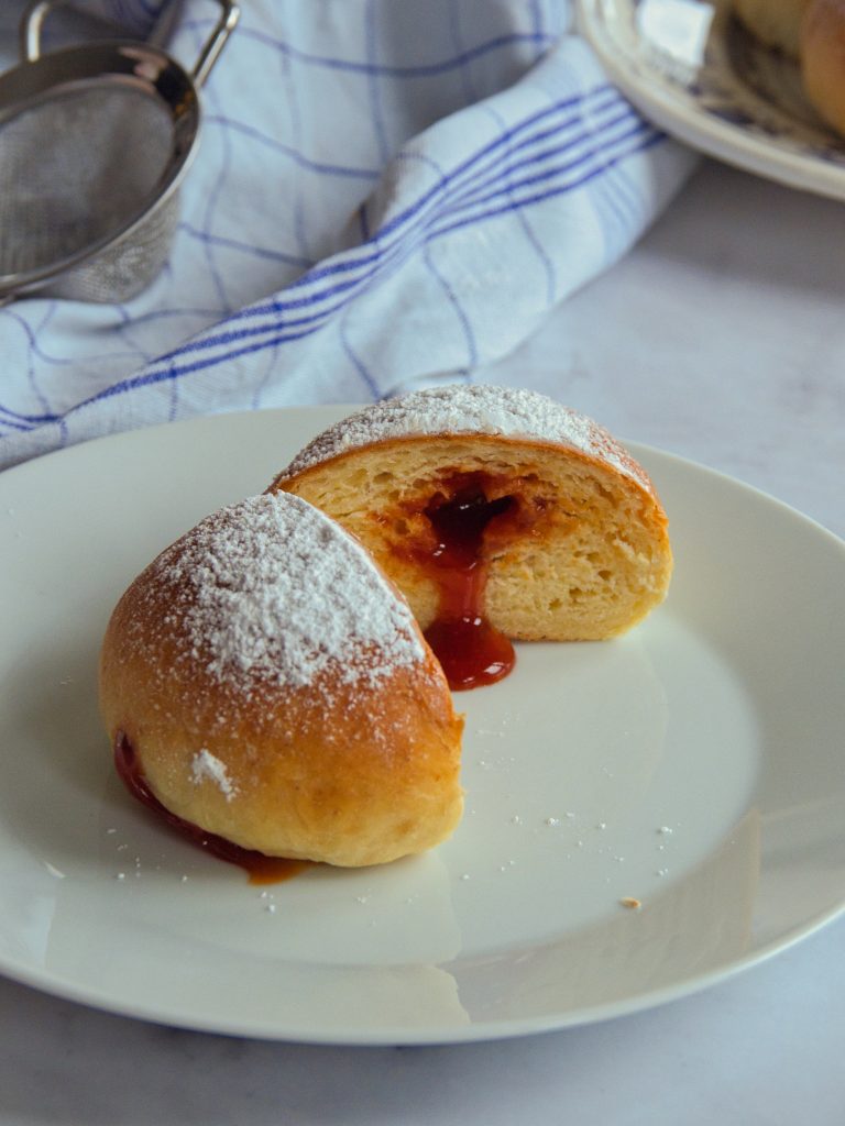 Ein aufgeschnittener Krapfen auf einem Teller bei dem Marmelade herausläuft.